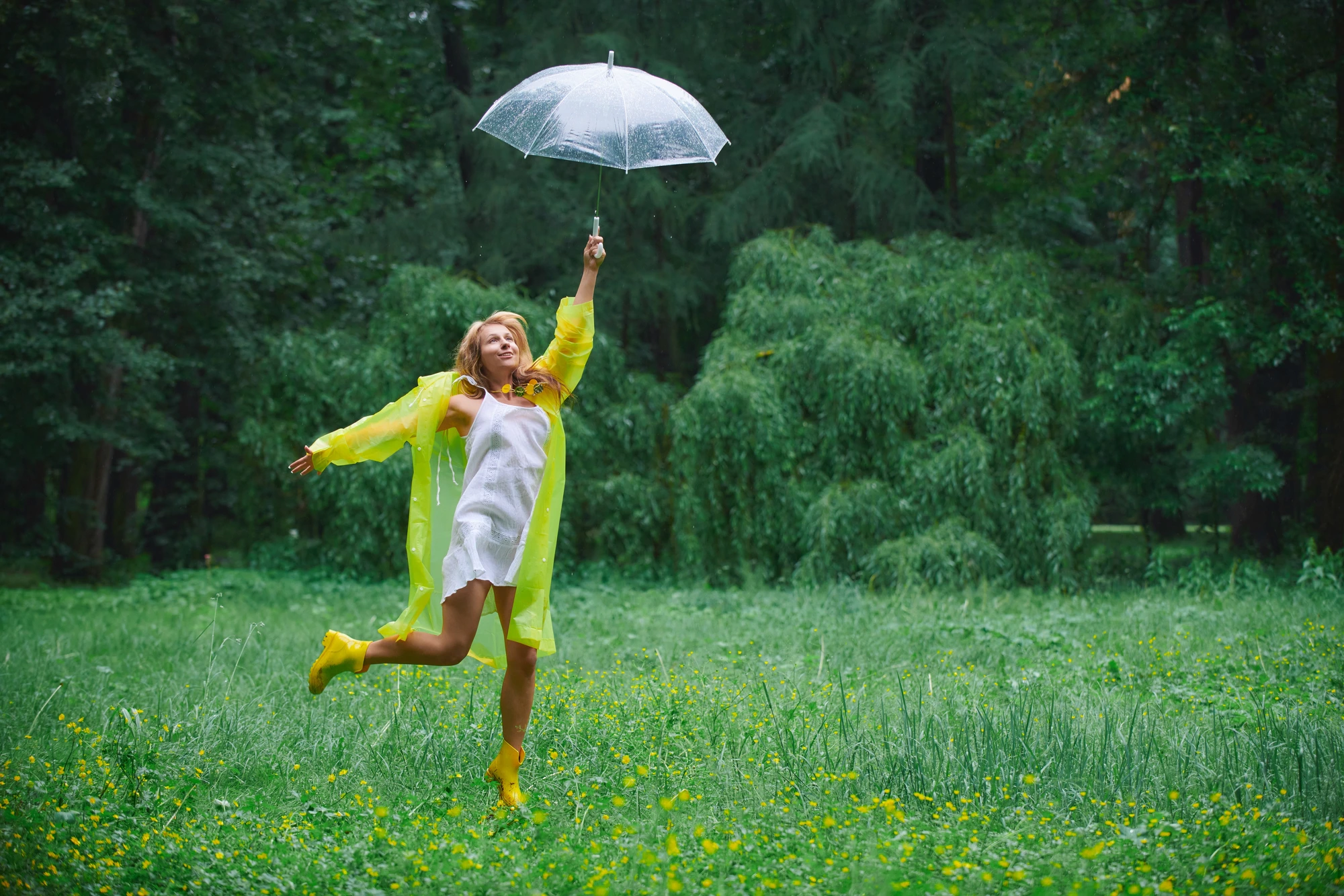 Femme joyeuse dansant sous la pluie avec un parapluie transparent, entourée de verdure